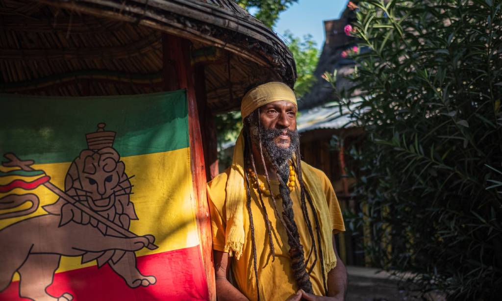 Homme devant un drapeau rastafari coloré.